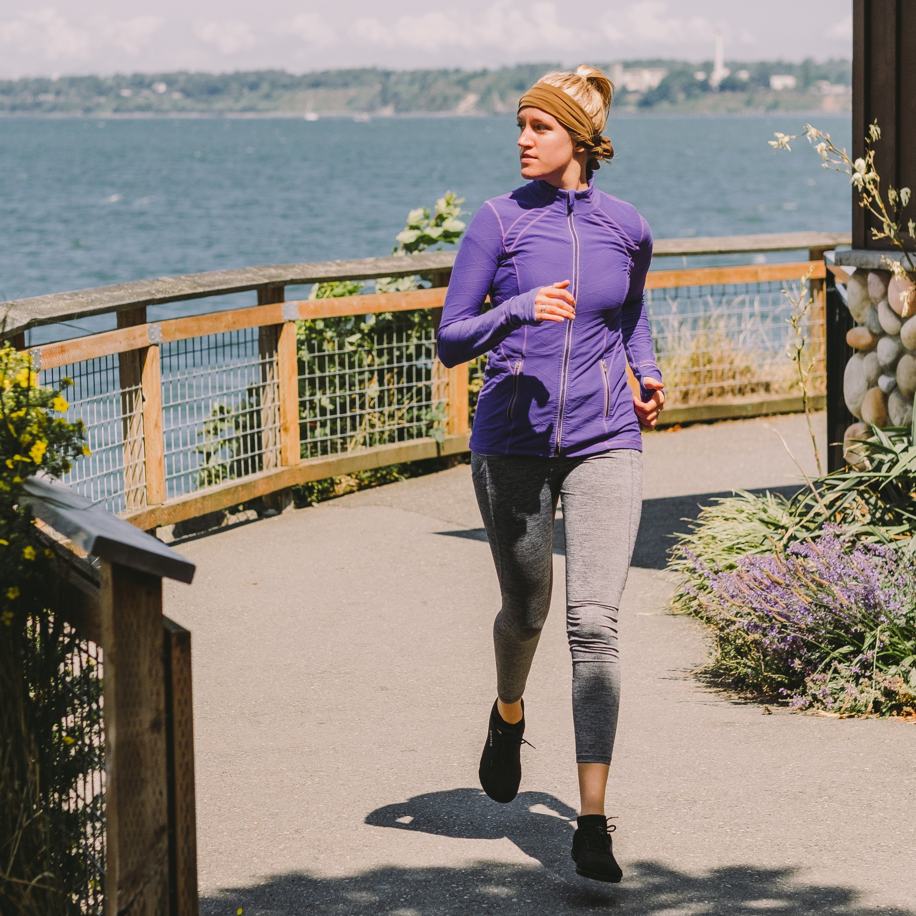 Person with a cooling towel wrapped around their head like a bandana running on a boardwalk with a bay in the background